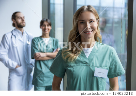 Woman physician standing near window in clinic with medical colleagues on background 124023218