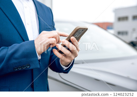 Businessman in suit holding smartphone at dealership Businessman in suit holding smartphone at dealership 124023252