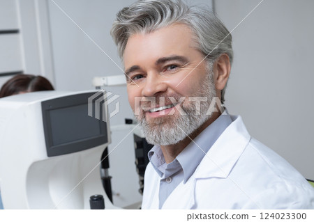Professional optometrist in clinic sitting at workplace with advanced technology 124023300
