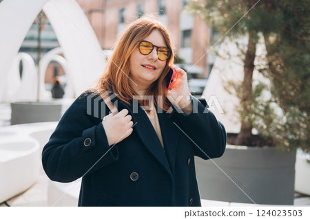 Happy 30s woman talking phone and look happy outdoors. Urban lifestyle concept. Spring time. Beautiful woman walking on the modern city street. Happy 30s woman talking phone and look happy outdoors. Urban lifestyle concept. Spring time. Beautiful woman walking on the modern city street. 124023503