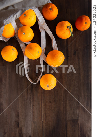 fresh unpeeled oranges placed in reusable nature textile bag on brown table. 124023522