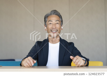 A man in his 60s wearing earphones talking while looking at the camera A man in his 60s wearing earphones talking while looking at the camera 124023577