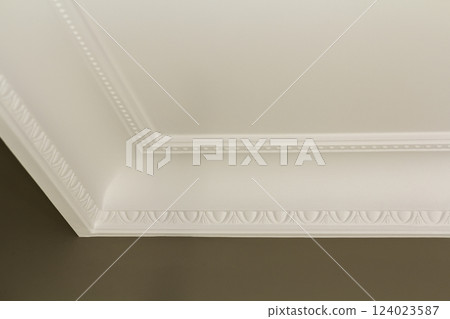 Ornamental white molding decor on ceiling of white room close-up detail. Interior renovation and construction concept. 124023587