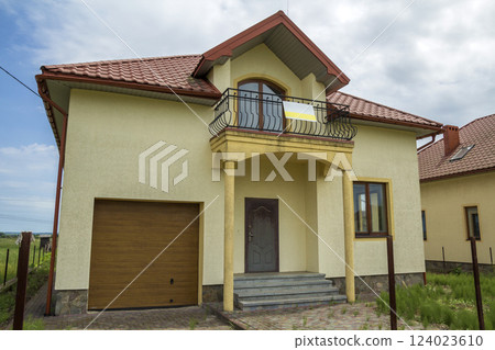 New yellow two-story residential cottage with shingle roof, front porch, plastic windows, high chimneys, balconies on blue sky background. Real estate property, architecture and prosperity concept. New yellow two-story residential cottage with shingle roof, front porch, plastic windows, high chimneys, balconies on blue sky background. Real estate property, architecture and prosperity concept. 124023610