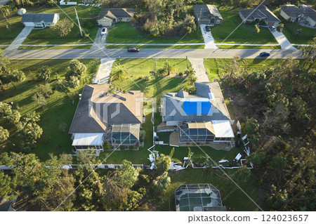 Leaking house roof covered with protective tarp sheets against rain water leaks until replacement of asphalt shingles. Damage of building rooftop as aftermath of hurricane Idalia in Florida 124023657