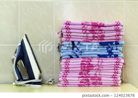 Ironing linen with steam generator. A stack of ironed towels lying next to the iron. Teflon sole plate covered with small holes. 124023676