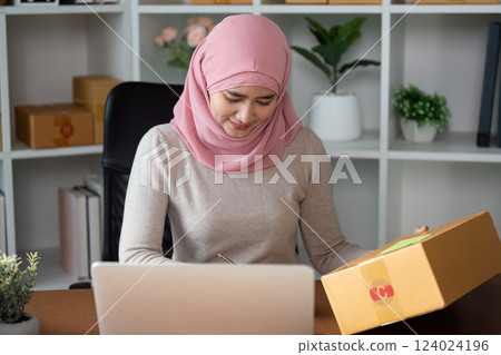Muslim woman managing online sales and packaging orders at her home office. Muslim woman managing online sales and packaging orders at her home office. 124024196
