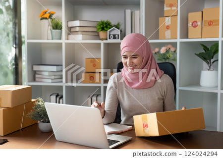 Happy Muslim woman engaged in online business while managing inventory and orders. Happy Muslim woman engaged in online business while managing inventory and orders. 124024294
