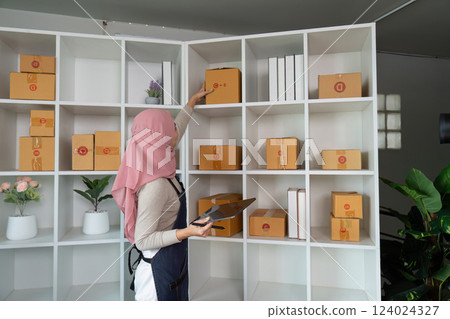 Muslim woman organizing packages on a shelf in her home office for online sales. Muslim woman organizing packages on a shelf in her home office for online sales. 124024327