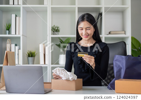Asian woman unboxing online purchase with credit card in hand Asian woman unboxing online purchase with credit card in hand 124024397