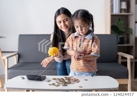 Mother and daughter counting coins together while learning about saving money in a modern living room. Mother and daughter counting coins together while learning about saving money in a modern living room. 124024457