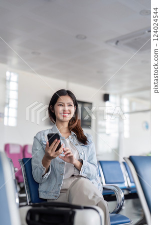 Cheerful young woman waiting in airport lounge while using smartphone for flight information Cheerful young woman waiting in airport lounge while using smartphone for flight information 124024544