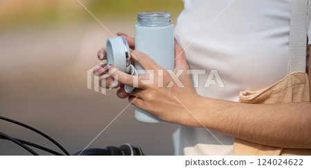 Close-up of a woman holding a reusable water bottle, promoting sustainability. Close-up of a woman holding a reusable water bottle, promoting sustainability. 124024622