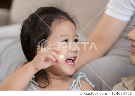 Joyful Childhood Moments and Snack Time. A little girl excitedly enjoys popcorn while interacting with a family member. 124024736