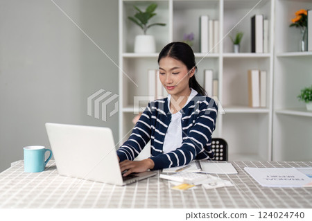 Cheerful woman reviewing bills and receipts at home, managing her finances with a positive outlook. Cheerful woman reviewing bills and receipts at home, managing her finances with a positive outlook. 124024740