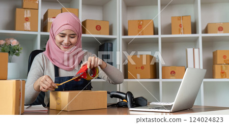 Muslim woman packing orders with tape in a home office for online business. 124024823