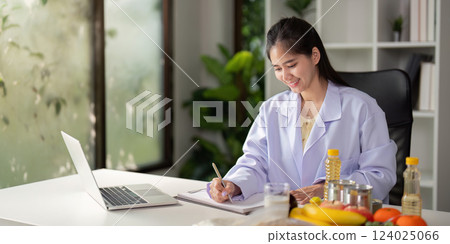 Nutritionist at Work. Female nutritionist analyzing diet plans with fresh produce and data charts. 124025066
