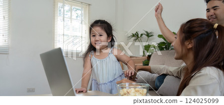 Family Bonding and Leisure Time. A young girl shares joyful moments with her parents while watching a movie together. Family Bonding and Leisure Time. A young girl shares joyful moments with her parents while watching a movie together. 124025099