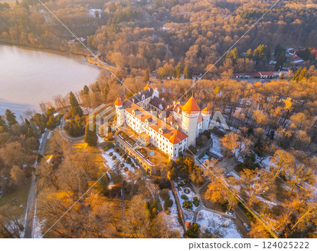 Konopiste Castle, surrounded by lush trees, stands proudly near a tranquil lake in Czechia. The warm light captures the historic architecture and serene landscape, showcasing its beauty. 124025222