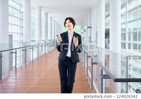 A businesswoman in a suit operating a smartphone while moving around the office 124026342