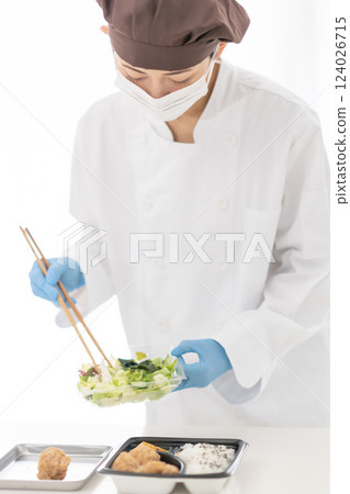 A woman wearing a mask arranges side dishes in a bento box 124026715