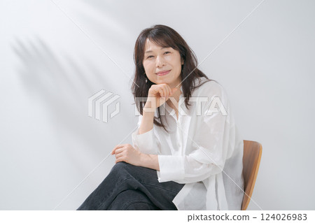 A smiling woman in her 50s sitting on a chair 124026983