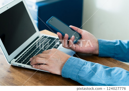 A man operating a smartphone and a computer 124027776