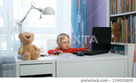 Cute baby girl at her work desk, focused on a laptop and taking notes, surrounded by toys and teddy bears. Freelance work concept 124028809