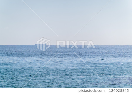 Calm blue sea with the silhouette of a large ship on the horizon Calm blue sea with the silhouette of a large ship on the horizon 124028845