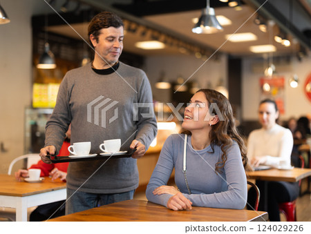 Man with two cups of coffee asks permission to sit at a table next to girl in a cafe 124029226