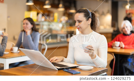 Woman surfing Internet on notebook while drinking tea or coffee in cafeteria 124029275