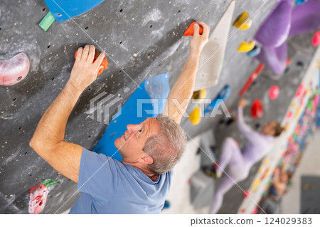 Alpinist practicing indoor rock climbing on artificial boulder without safety belts 124029383