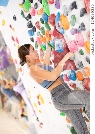 Concentrated young girl climbing on bouldering wall in gym 124029389