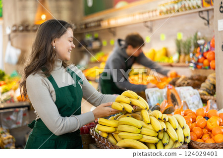 Young female seller holding bananas standing by counter in grocery market 124029401