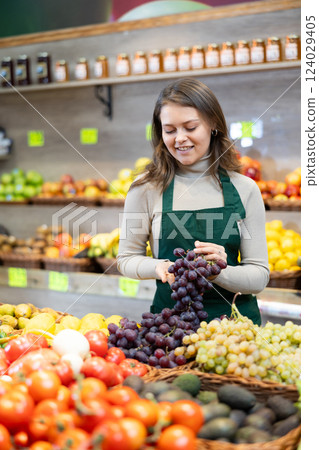 Young female seller in apron displaying assortment of grape at supermarket 124029405