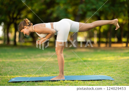 Girl in park on green grass of lawn performs Natarajasana Girl in park on green grass of lawn performs Natarajasana 124029453