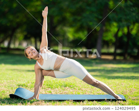 Girl in park on green grass of lawn performs Utthita Parshvakonasana 124029495