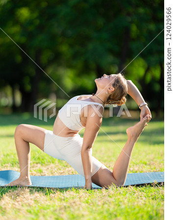 Sporty girl performing Crescent Low Lunge Pose on green meadow Sporty girl performing Crescent Low Lunge Pose on green meadow 124029566
