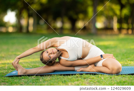 Girl in park on green grass of lawn performs Parivritta Janu Shirshasana Girl in park on green grass of lawn performs Parivritta Janu Shirshasana 124029609