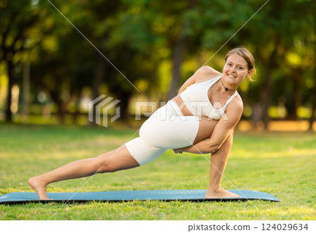 Girl in park on green grass of lawn performs Parivritta Parshvakonasana Girl in park on green grass of lawn performs Parivritta Parshvakonasana 124029634