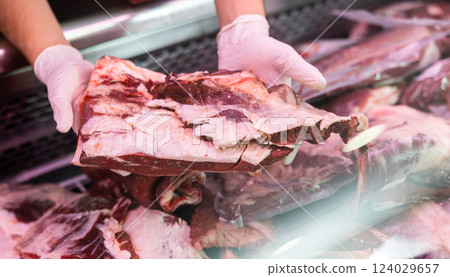 Row piece of meat held in hands by seller against background of showcase of butcher shop Row piece of meat held in hands by seller against background of showcase of butcher shop 124029657