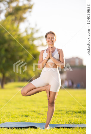 Girl doing Vrikshasana balancing yoga asana on green meadow Girl doing Vrikshasana balancing yoga asana on green meadow 124029688