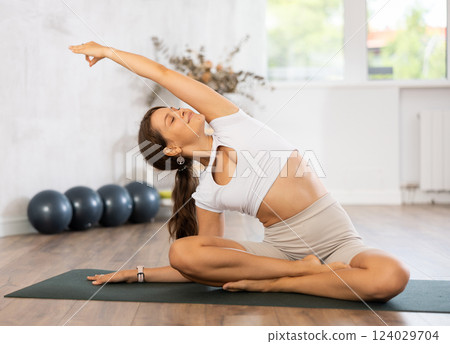 Young woman yoga trainer performing lotus pose variation on black rug Young woman yoga trainer performing lotus pose variation on black rug 124029704