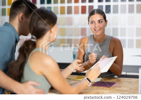 Female saleswoman of paintwork material shop advises spouses buyer with samples and product catalog 124029706
