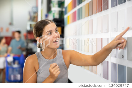 Near stand with samples paint, palette of colors of coating, woman buyer examines showcase in store 124029747