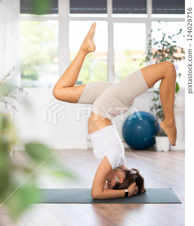 Experienced girl fitness club teacher performs feathered peacock asana, pincha mayurasana 124029756