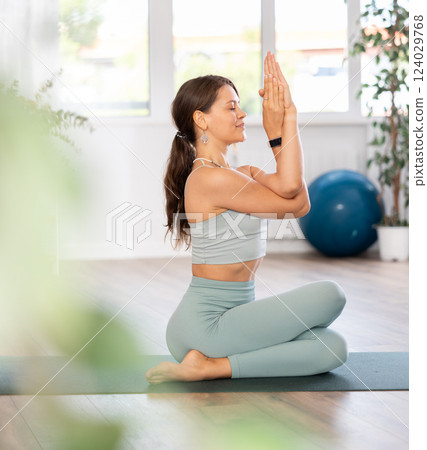 Young woman yoga trainer performing eagle pose on black rug 124029768