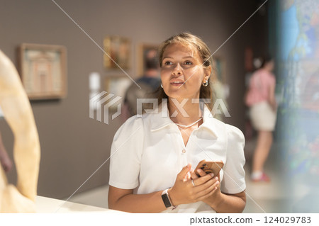 Girl with phone in hands walks around museum hall, view exhibition items 124029783