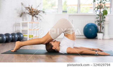 Experienced girl fitness club teacher performs plough plow asana, halasana Experienced girl fitness club teacher performs plough plow asana, halasana 124029794