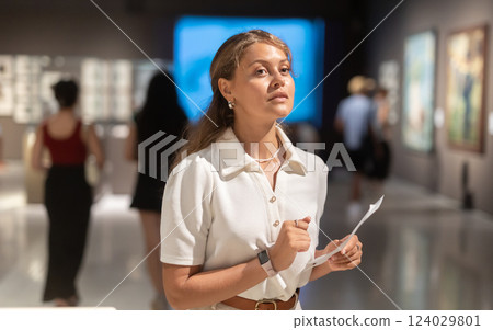Woman with sheet piece of paper in hands view pictures and icons in museum hall 124029801